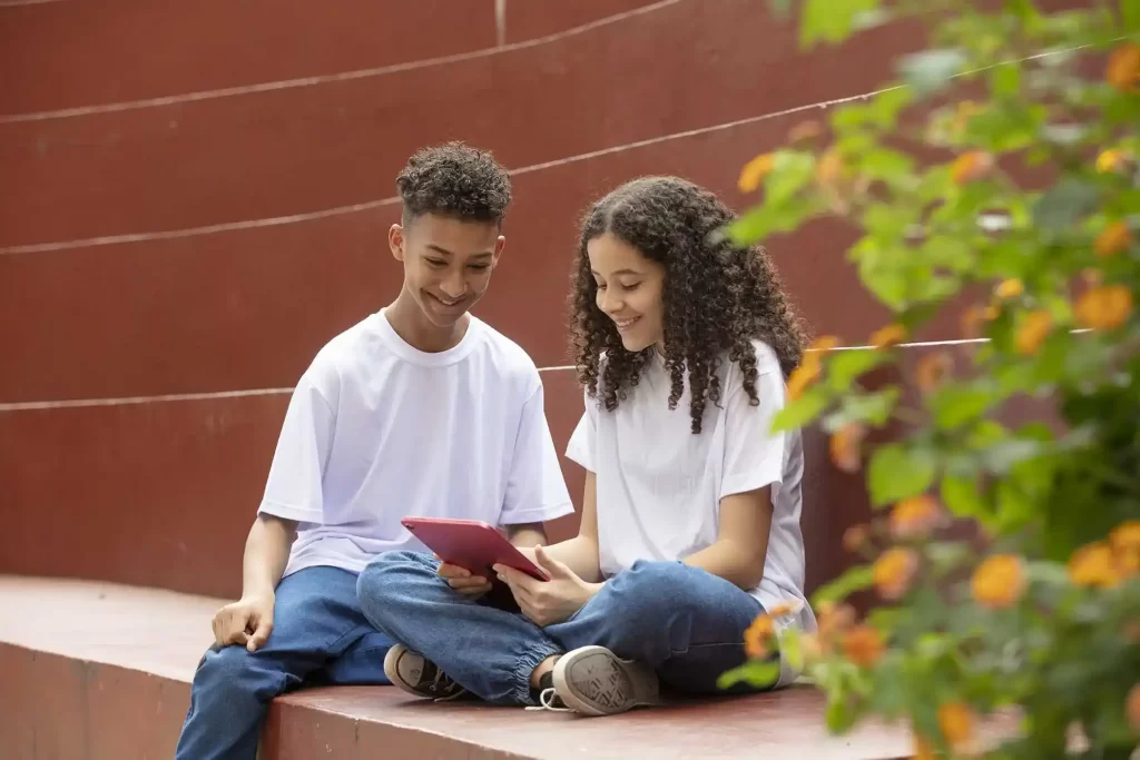 Jovens sentados em degraus externos sorrindo enquanto olham para um tablet vermelho.