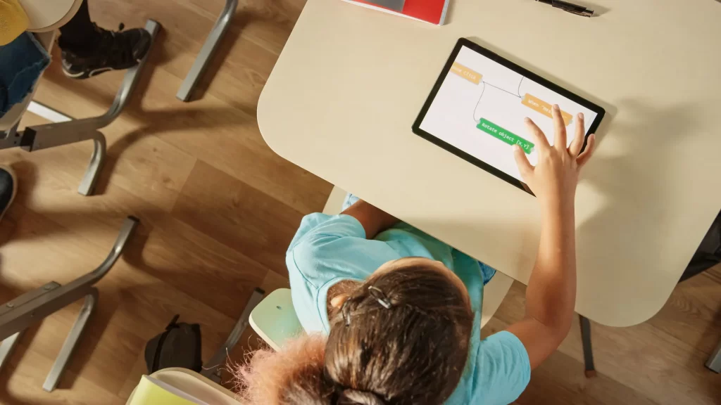 Aluna da geração alpha utiliza tecnologia em tablet na escola para atividades digitais.